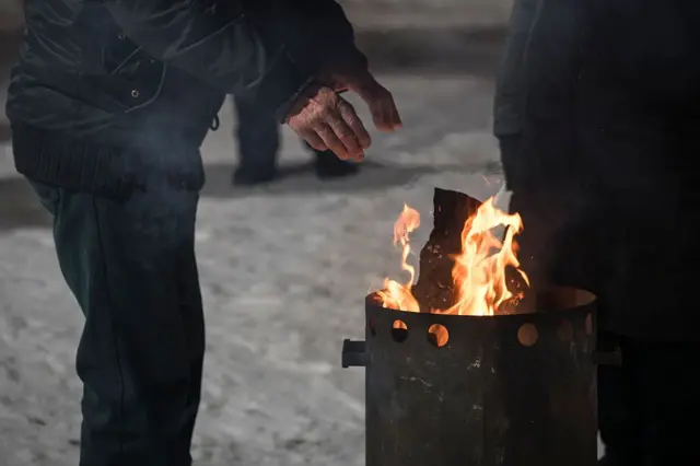 Люди зігріваються біля палаючої бочки на снігу взимку