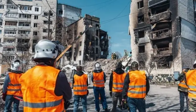 Національні бригади відновлення біля зруйнованих будівель у помаранчевих жилетах