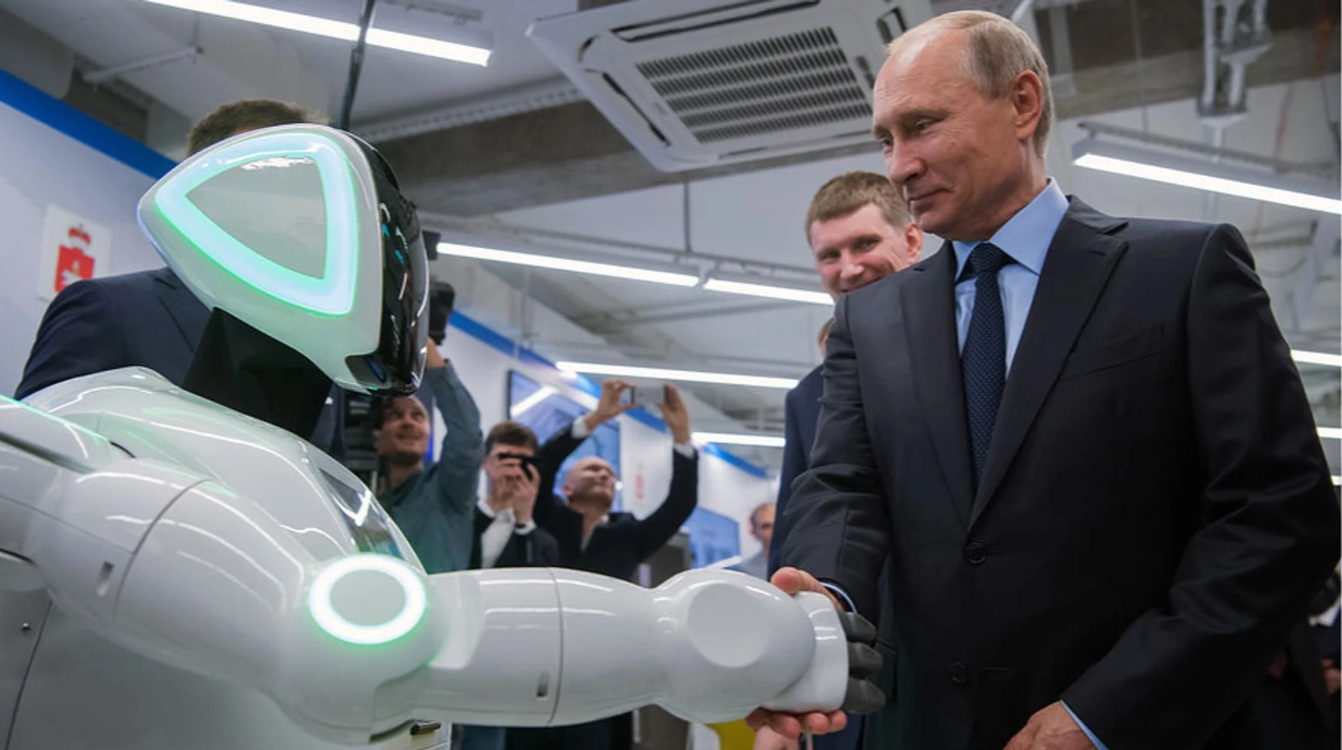Путін тисне руку білому гуманоїдному роботові з зеленим підсвічуванням серед журналістів