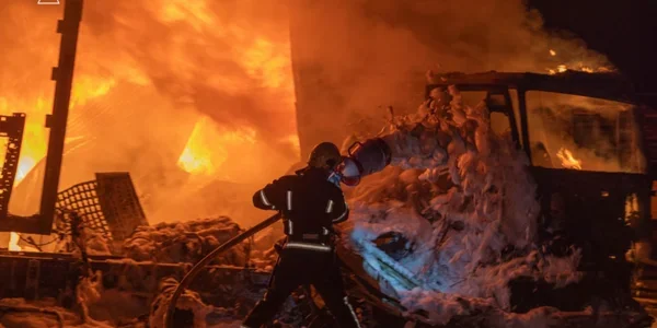 Пожежник у спорядженні гасить піною палаючу вантажівку вночі серед полумя
