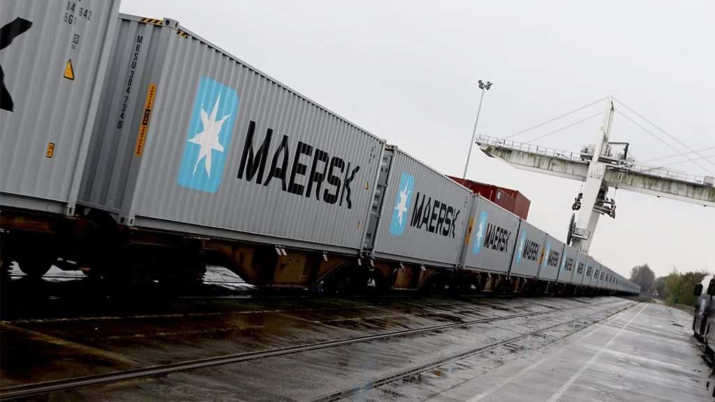 Потяг із контейнерами Maersk на мокрих коліях біля портового крана